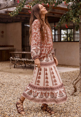a-woman-wearing-a-bohemian-style-two-piece-dress-set-with-a-rust-brown-and-cream-floral-pattern-walking-outdoors-on-a-gravel-path-near-a-patio
