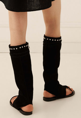black-over-the-knee-leg-warmers-with-silver-stud-detailing-at-the-top-worn-by-a-model-with-black-slide-sandals-on-a-light-beige-background